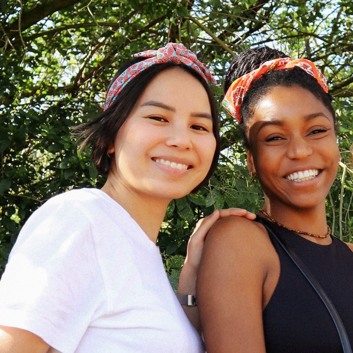 Femme souriante portant un bandeau vert à motif floral rouge, photographiée en terrasse de café. Accessoire cheveux tendance, style naturel et lumineux, idéal pour mettre en valeur un look casual chic.